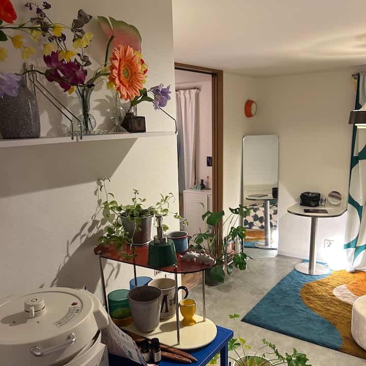 明るいベージュトーンのリビングとキッチン空間、多彩な花瓶と植物が配置された雰囲気のあるインテリア