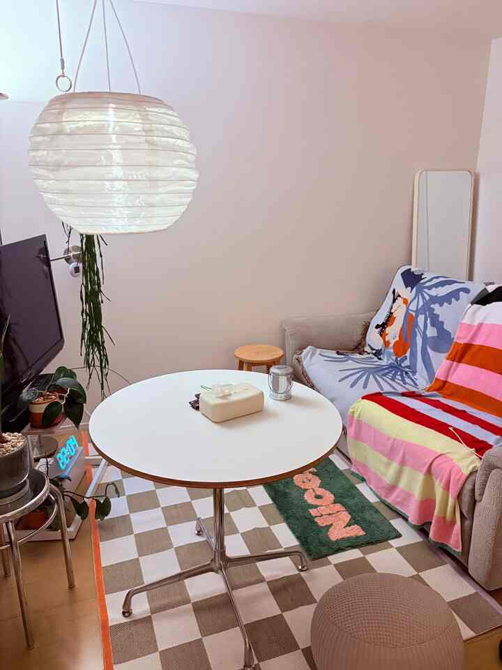 ナチュラルなベージュ色調の狭いリビング、丸い白テーブルとグレーのソファ、ホワイトのペンダントライトが温かみのある雰囲気を演出しているインテリア