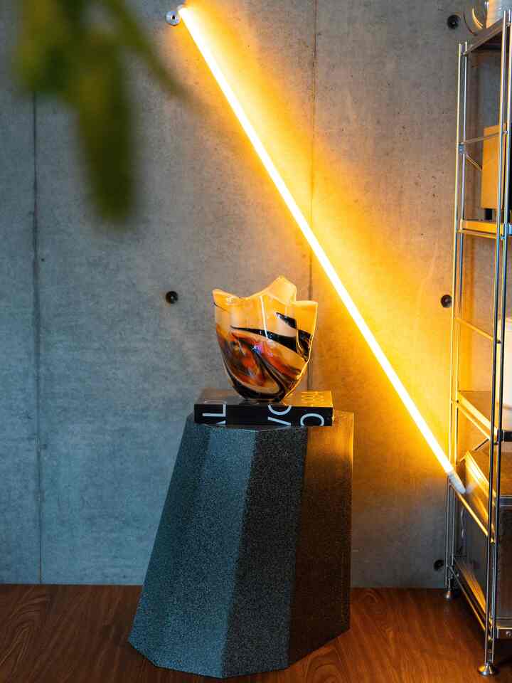 Minimal kitchen interior featuring a vintage glass vase on a gray stool with yellow neon light accent