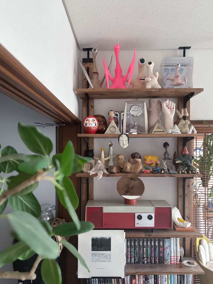 白い壁に囲まれたナチュラルウッドのコーナー収納、アート作品とコレクションが並ぶ印象的な空間