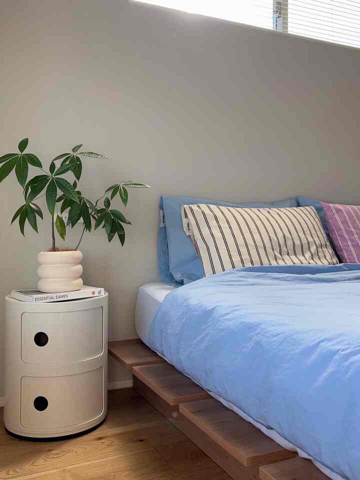 Natural color and blue toned bedroom with wood tone bed frame, side table and green plant arranged neatly