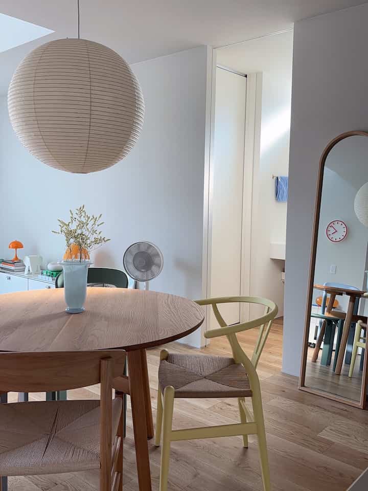 Natural wood tone and white dining room featuring orange accent decor and a BALMUDA GreenFan, creating a clean space