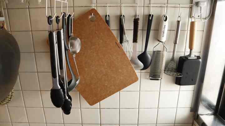 ナチュラルなブラウンのまな板と様々な調理器具が白いタイルの壁に掛けられた整然としたキッチンのインテリア