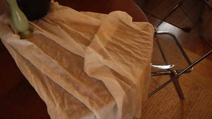 茶色の床と白いテーブルクロスのあるダイニング、透明なプラスチックチェアが配置された温かみのあるインテリア