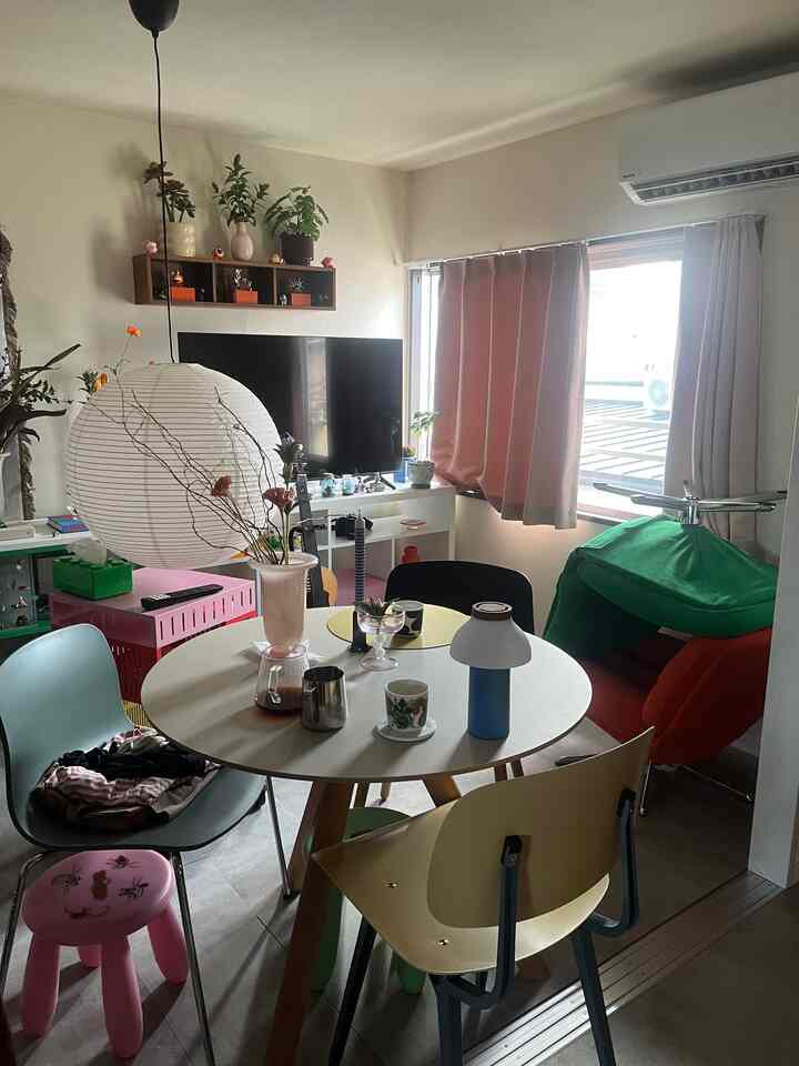 自然光が差し込む白い壁と丸いダイニングテーブル、多様な椅子と植物が配置されたミッドセンチュリーモダン風の居心地の良い1LDKリビング