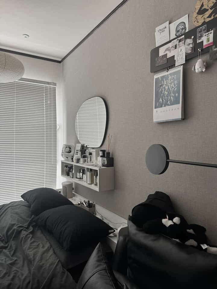 Gray tone bedroom featuring dark gray bedding, wall lamp, and a wall-mounted mirror in a minimal setting