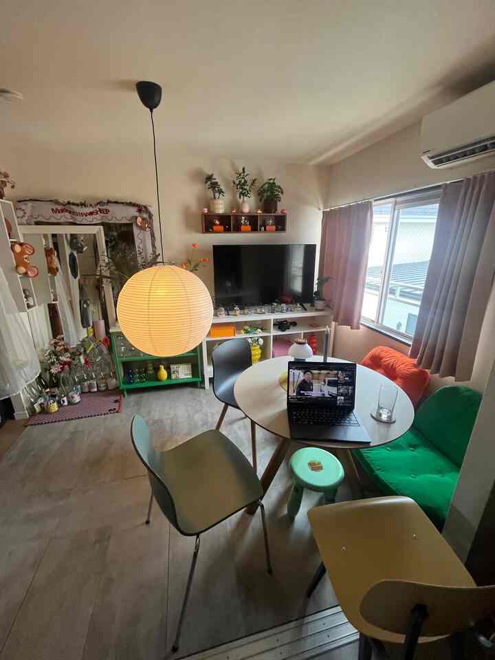 明るいベージュ色の壁の1LDKリビング、丸いダイニングテーブルにカラフルな椅子、大きな丸型ペンダントライトが配置された雰囲気のあるインテリア