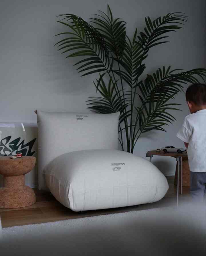 White and natural color toned living room featuring a large cushioned sofa, cork stools, and a child playing nearby