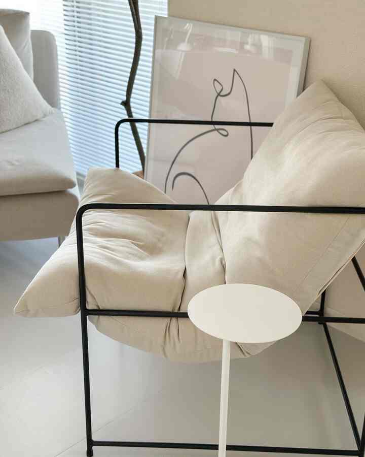 ベージュトーンのリビング、金属フレームのアームチェアと小さな丸い白いサイドテーブルが配置された印象的なインテリア