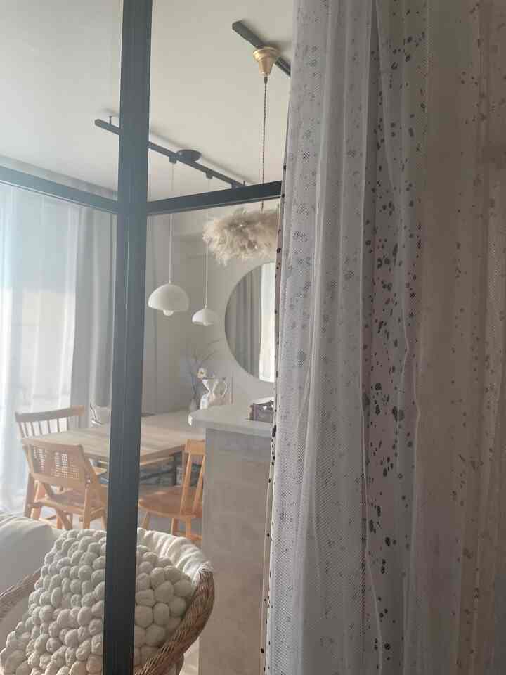 アイボリーと木目調の小さなリビングルーム、カーテンとラタンチェアが配置された落ち着いた自然な雰囲気のインテリア