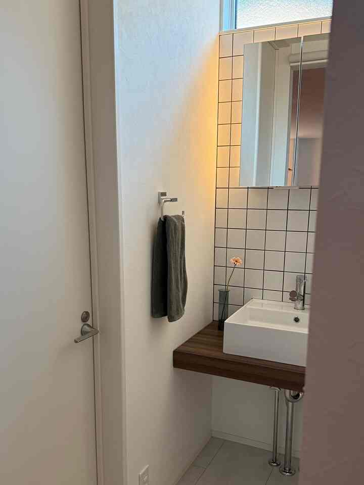 白とナチュラルトーンのバスルーム洗面台、鏡と小さな花瓶が配置された印象的な空間