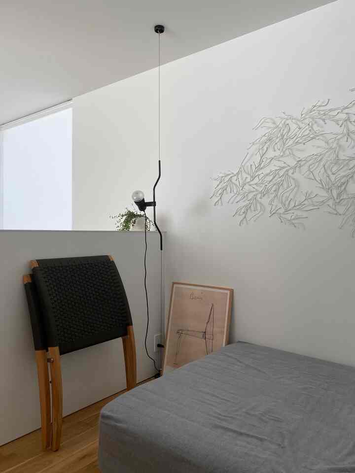 Modern kids' room with white walls and wood tone flooring, featuring a gray bedspread and folded armchairs in a minimalist setting