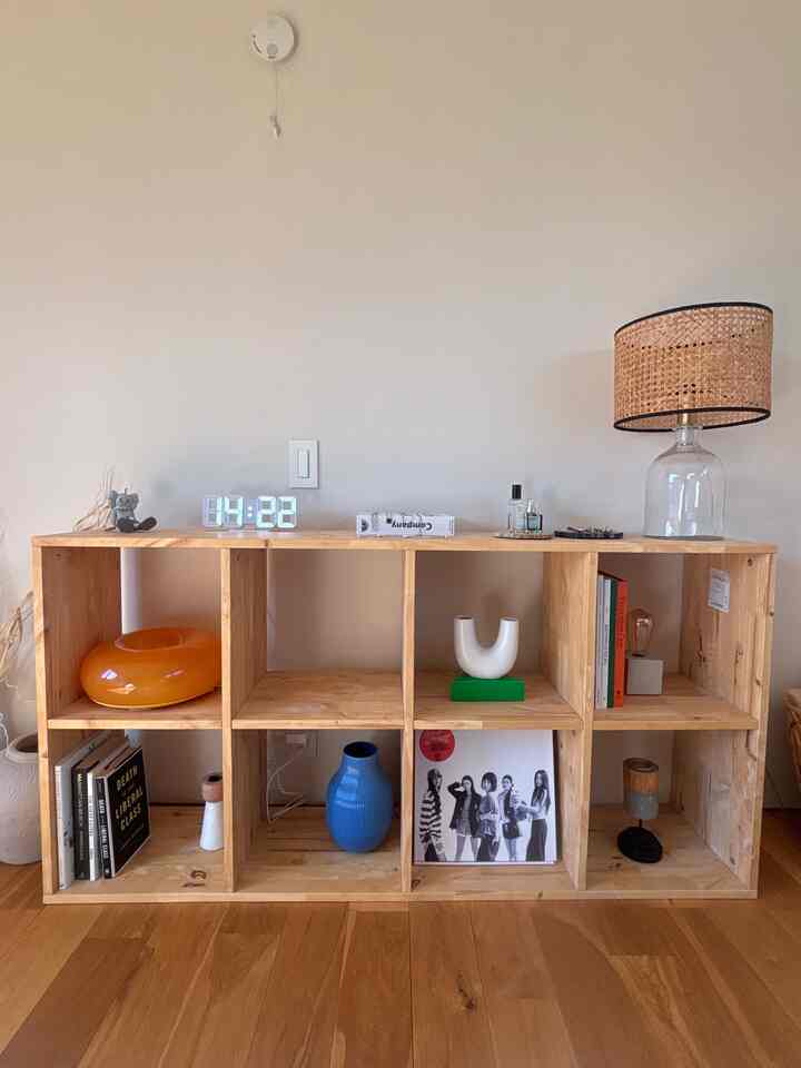 温かみのある木目調の多目的リビング本棚に、デジタル時計、青い花瓶、ラタンのテーブルランプが配置された韓国インテリアの印象的な空間