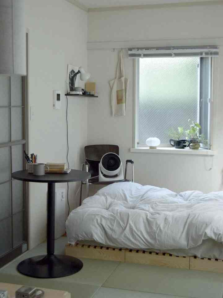 Bright white tone bedroom featuring natural wood bed frame and plants by the window creating a cozy atmosphere.