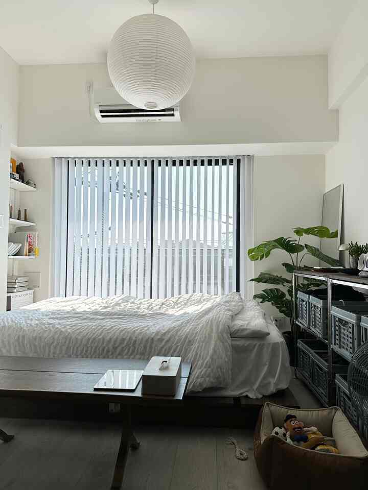 White and light gray toned bedroom featuring a large central bed with vertical blinds, neat mid-century modern style space