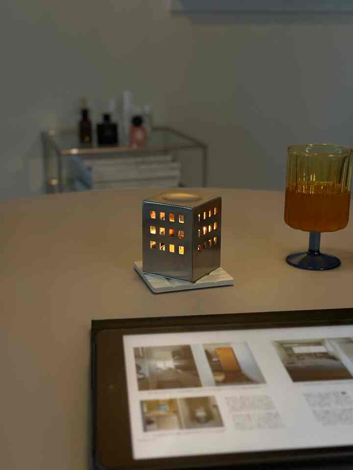 モダンなベージュトーンのダイニングに、中央に銀色のキャンドルホルダーと黄色いガラスが配置され、手前にタブレットで読書する空間