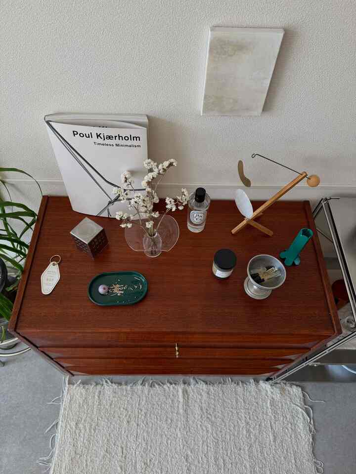 ナチュラルな色調のリビング、ヴィンテージ木製チェストの上にラグ、モビール、キャンドル、インセンスホルダーが配置された雰囲気のあるインテリア