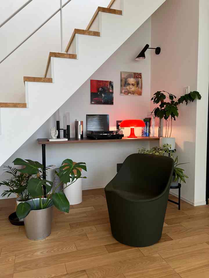 木目調の床と階段があるミッドセンチュリーモダンな二人暮らし空間、レコードプレーヤーと赤い照明が配置された印象的なコーナーに植物と椅子があるアットホームなインテリア