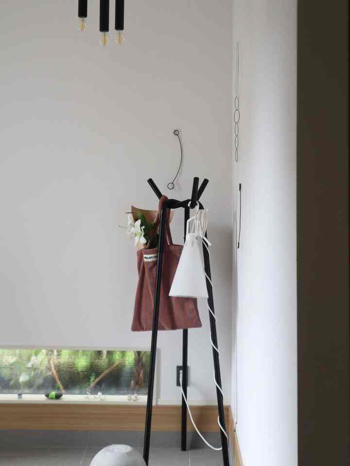 白い壁と黒のコートハンガー、バッグの中の白い百合が印象的なミニマルな玄関の空間
