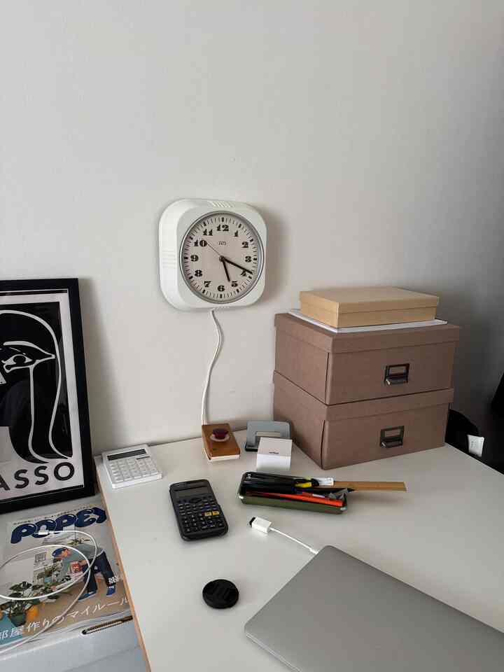 白い壁とデスク、時計と収納ボックスが配置された整ったホームオフィス空間