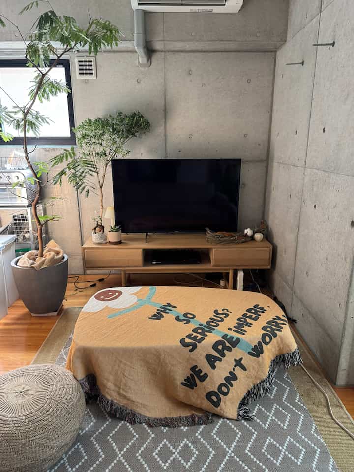 ナチュラルカラーのリビング、木目調のテレビ台とベージュのスローが掛けられたコーヒーテーブルが配置された印象的な空間