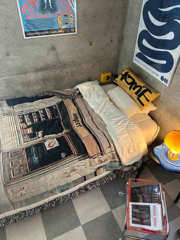 Brown and gray toned bedroom with concrete walls and posters, featuring yellow cushions and warm lighting in a cozy atmosphere
