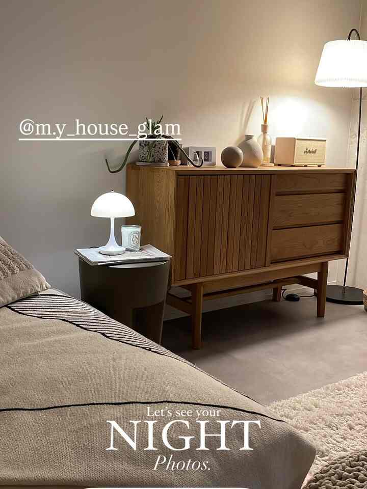 ベージュとホワイトの色調のリビング、ナチュラルな木製サイドボードとサイドテーブルにムードランプとキャンドルが置かれた落ち着きのあるインテリア