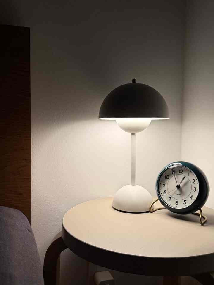 White-toned bedroom nightstand featuring a Flowerpot lamp and Arne Jacobsen table clock creating a simple, cozy atmosphere