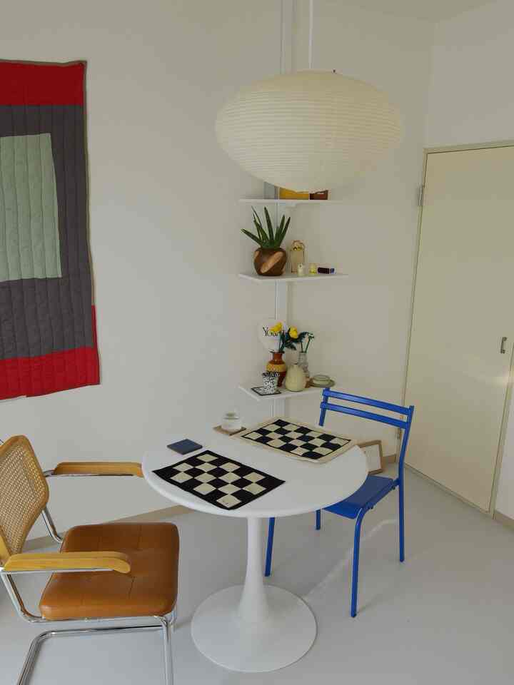 白を基調とし、青と茶色の椅子が配置されたミニマルなダイニングルーム、整然としたランチョンマットが印象的な空間