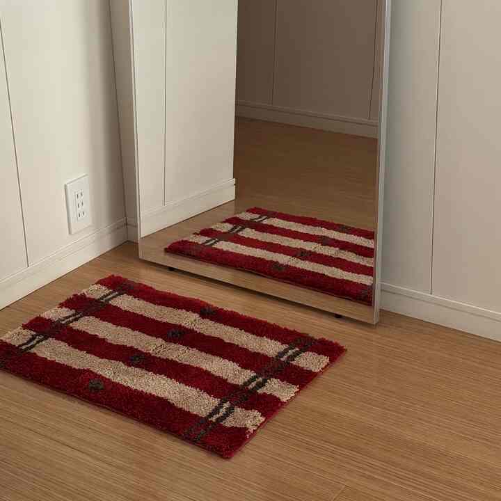 木目調の床と白い壁の玄関スペースに赤とベージュのストライプ柄のバスマットが置かれている