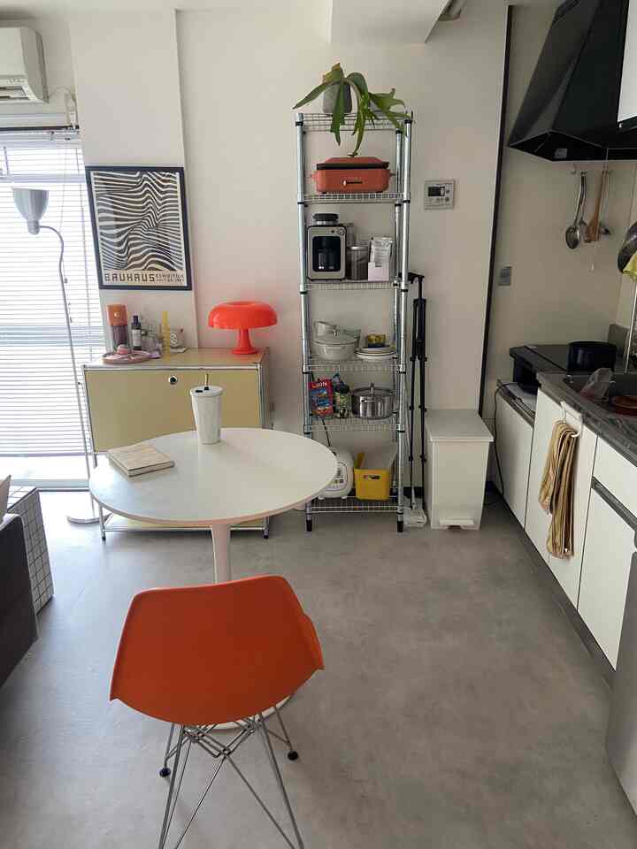 白とオレンジの色調が特徴の1DKキッチン兼ダイニング空間、ミッドセンチュリーモダンの椅子とランプが配置された清潔で実用的なインテリア