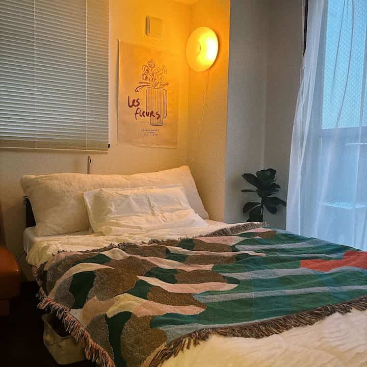 暖かいオレンジライトが灯る白い寝室、カラフルなスローと大きな植物が配置された雰囲気のある空間