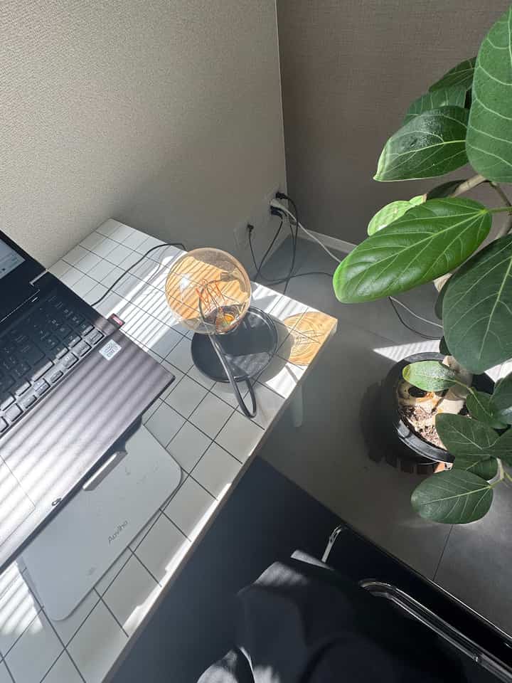 白いタイルのデスクとエジソンランプ、パソコンと観葉植物が配置されたモダンなホームオフィスのインテリア