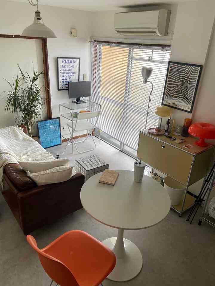 White and brown toned single household living room featuring mid-century modern furniture and compact home office setup with a simple atmosphere