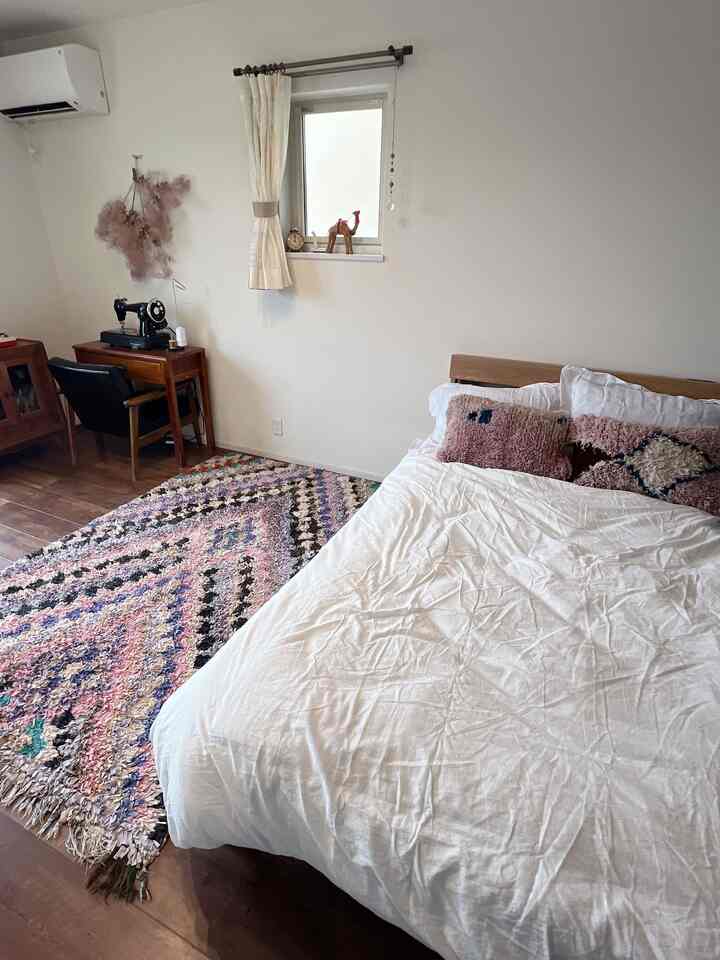 白い寝具と木製ベッドが配置された寝室、床にはボヘミアン風のモロッコ柄ラグが印象的な雰囲気のあるインテリア