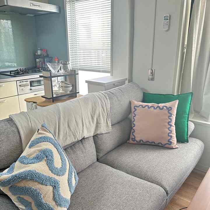 グレーとナチュラルカラーの1LDK空間、ソファとクッションが配置された落ち着いた雰囲気のインテリア