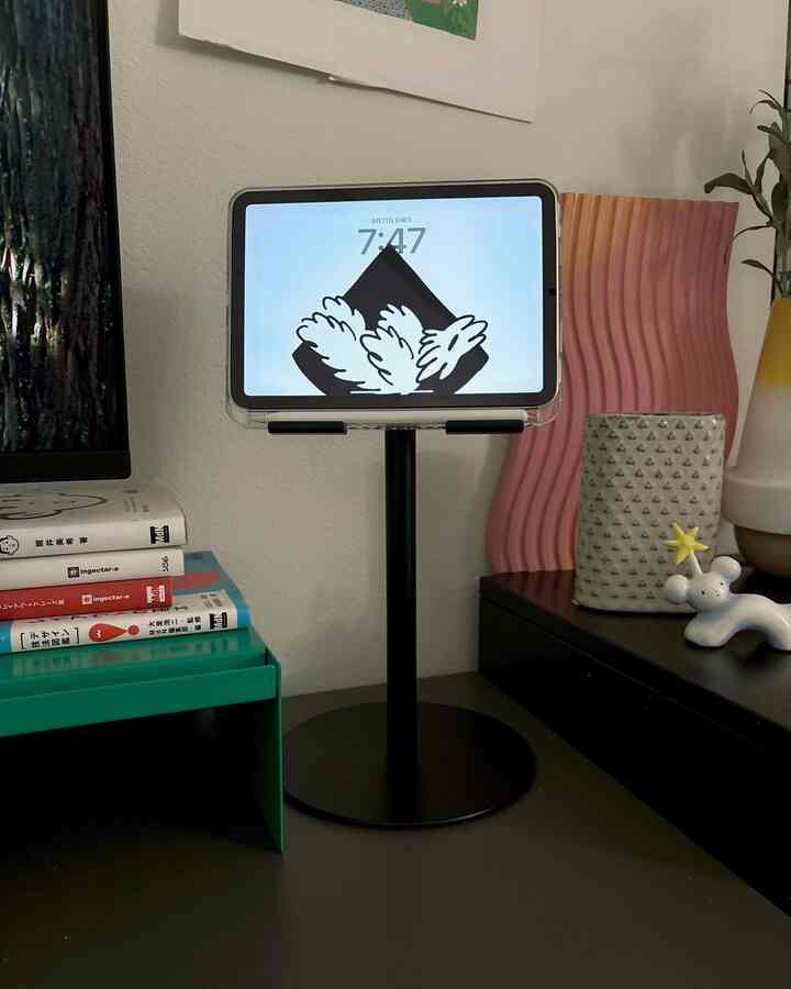 黒いモダンなデスクの上にシンプルなタブレットスタンドと小物が置かれた、清潔感のある一人暮らしのワークスペース