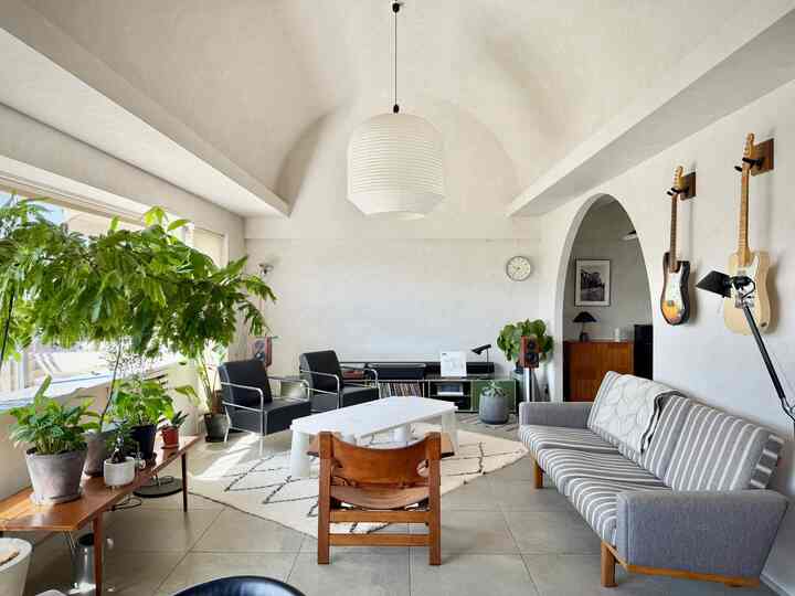 Bright and airy living room with white and natural tones, featuring vintage Mid-Century Modern furniture, plants, and arched interior elements