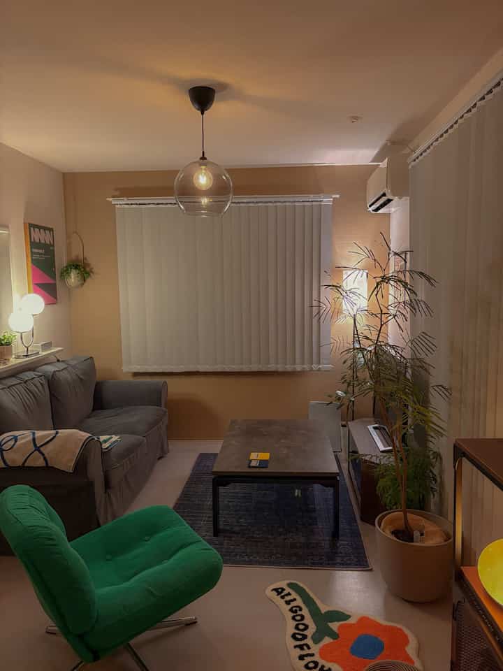 温かみのあるベージュの壁にグレーのソファと緑のアームチェア、植物が配置された雰囲気のあるリビング空間