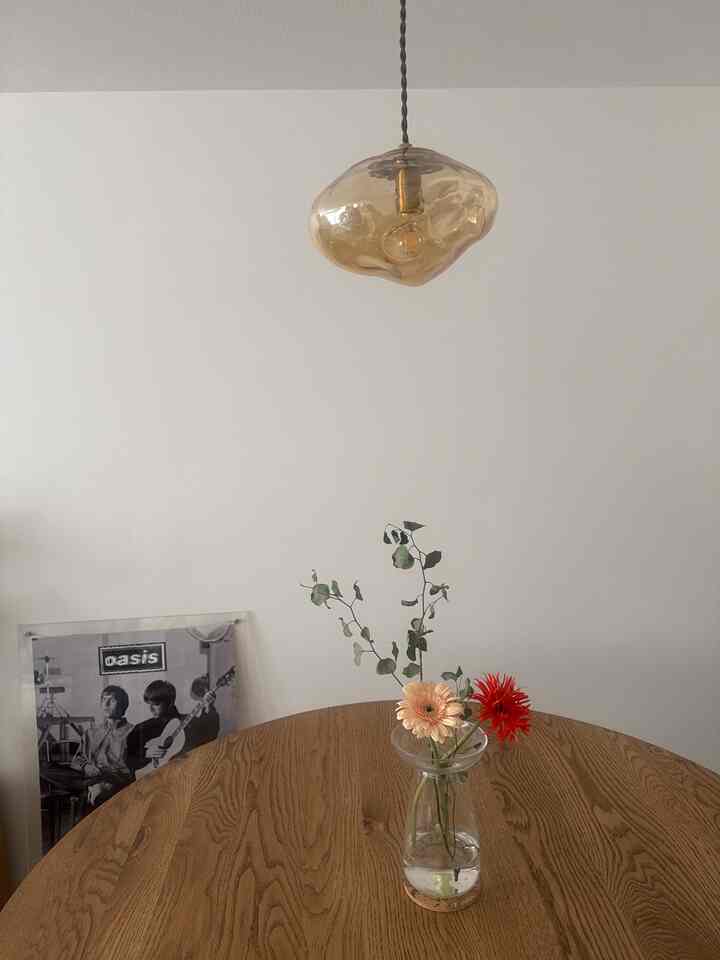 ナチュラルな色調のダイニングルーム、丸い木製のダイニングテーブルに花瓶と植物が置かれたシンプルな空間