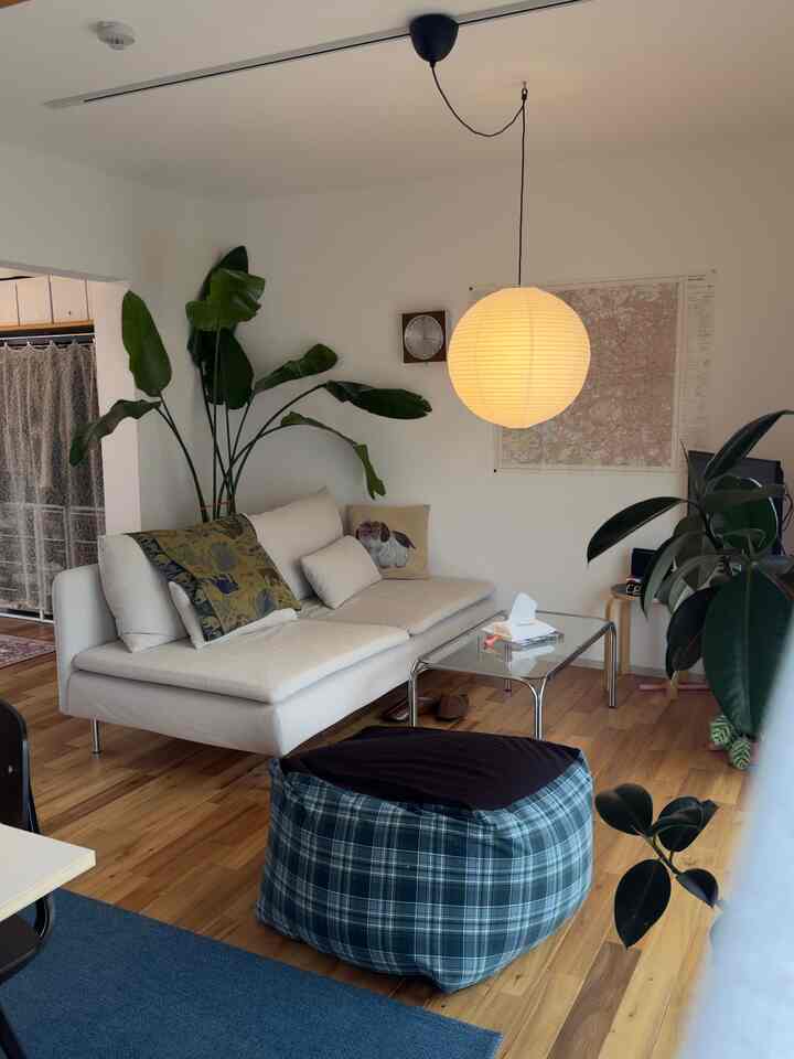 自然な木目調の床と大きな観葉植物がある、ベージュのソファとペンダントライトが配置された居心地の良いミニマルなリビング