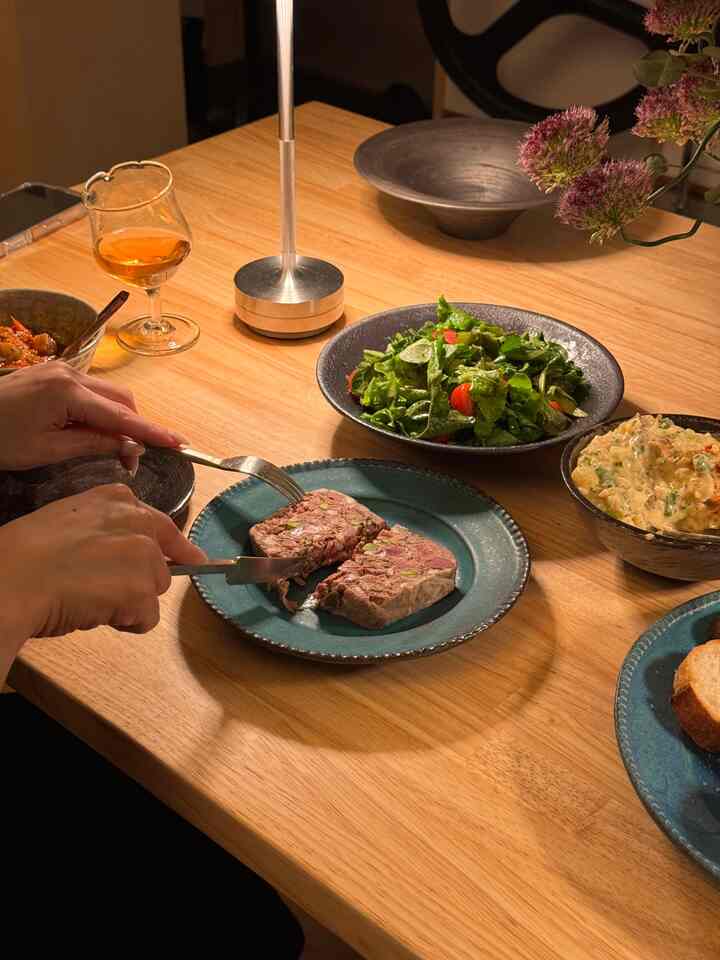 ナチュラルカラーの木製ダイニングテーブルに多様な器と料理が配置された落ち着いた一人暮らし空間