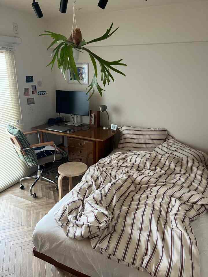 白と茶色の北欧風寝室、デスクとストライプの掛け布団カバーが配置された落ち着いたインテリア