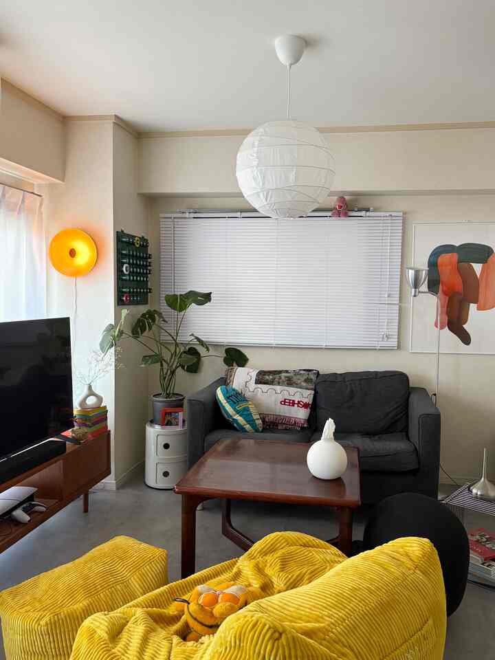 ホワイトとイエローの色調の1LDKリビング、中央に木製のコーヒーテーブルがあり、グレーのソファとイエローのアームチェアが配置された雰囲気のある空間