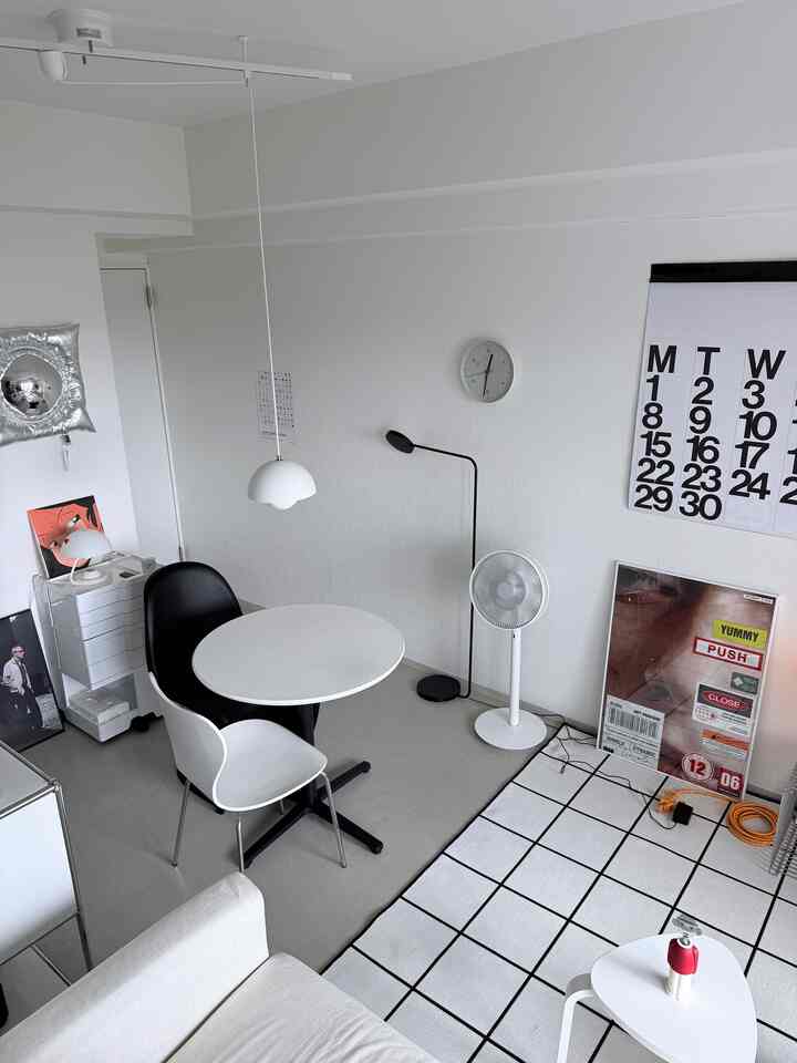 白と黒のトーンの1LDKリビングルーム、丸テーブルと2脚の椅子、大きなグリッド柄のラグが配置されたシンプルモダンなインテリア