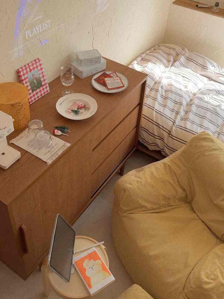 Beige and brown toned small bedroom featuring a large dresser and yellow bean bag sofa creating a cozy atmosphere.