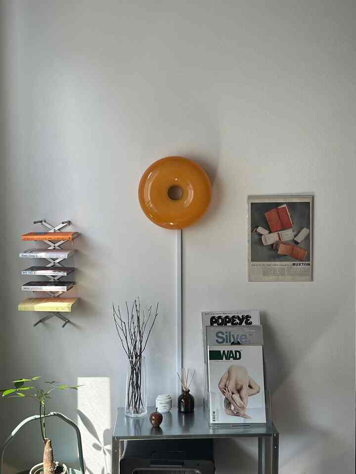 明るいナチュラルカラーの壁とオレンジの壁照明があるシンプルな1LDKリビング、植物と装飾的なオブジェが配置された空間