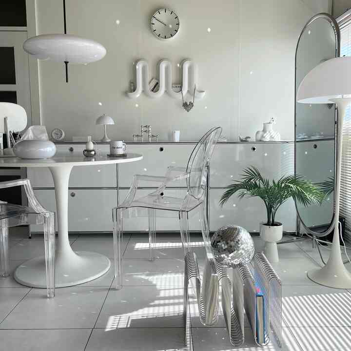 White-toned living room featuring transparent Louis Ghost armchairs, white Tulip table, floor lamp, and large standing mirror in a modern, clean space