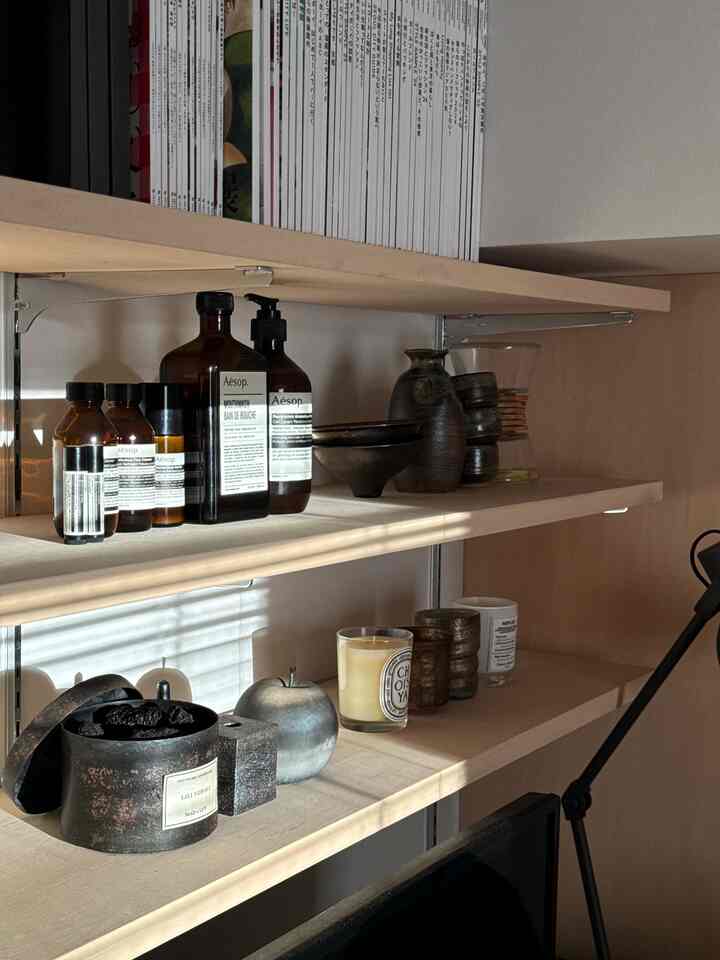ナチュラルなベージュトーンの棚にディフューザー、アロマキャンドル、ハンドバームが整然と配置された落ち着いた一人暮らしの空間