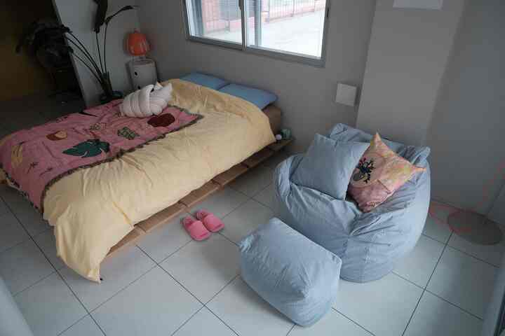 淡い黄色調の寝室、ベージュのベッドとパステルブルーのビーズソファが配置された居心地の良いインテリア